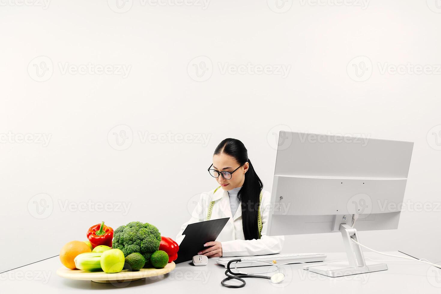 Female nutritionist working on computer at table in office. Expert makes healthy balanced diet plate according to proportions of nutrients. White background, copy space, ads photo