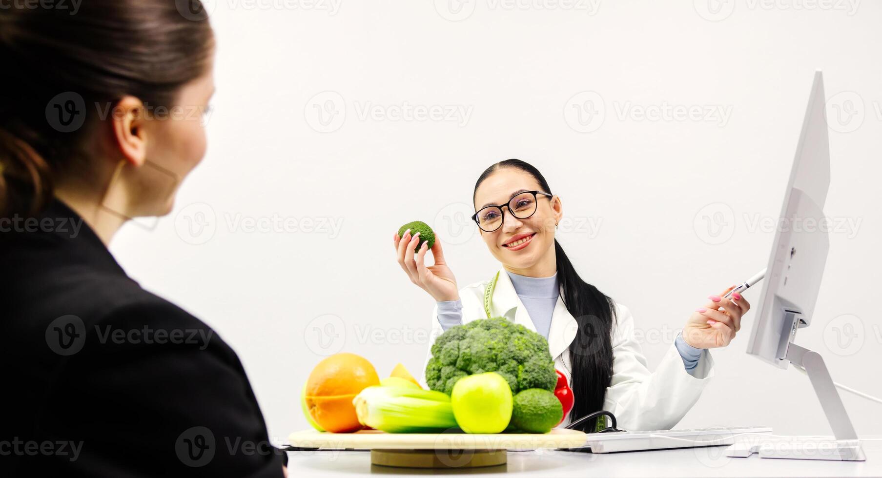 Woman professional nutritionist working and checking data on computer with a variety of fruits, nuts, vegetables, and dietary supplements on the table. White background photo