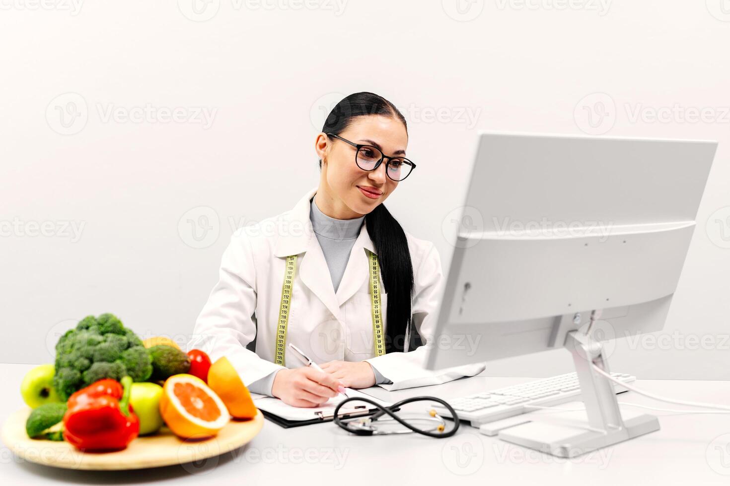 Woman doctor typing on modern laptop in consulting room of medical center. Experienced nutrition professional searching for weight loss information on food websites. White background photo