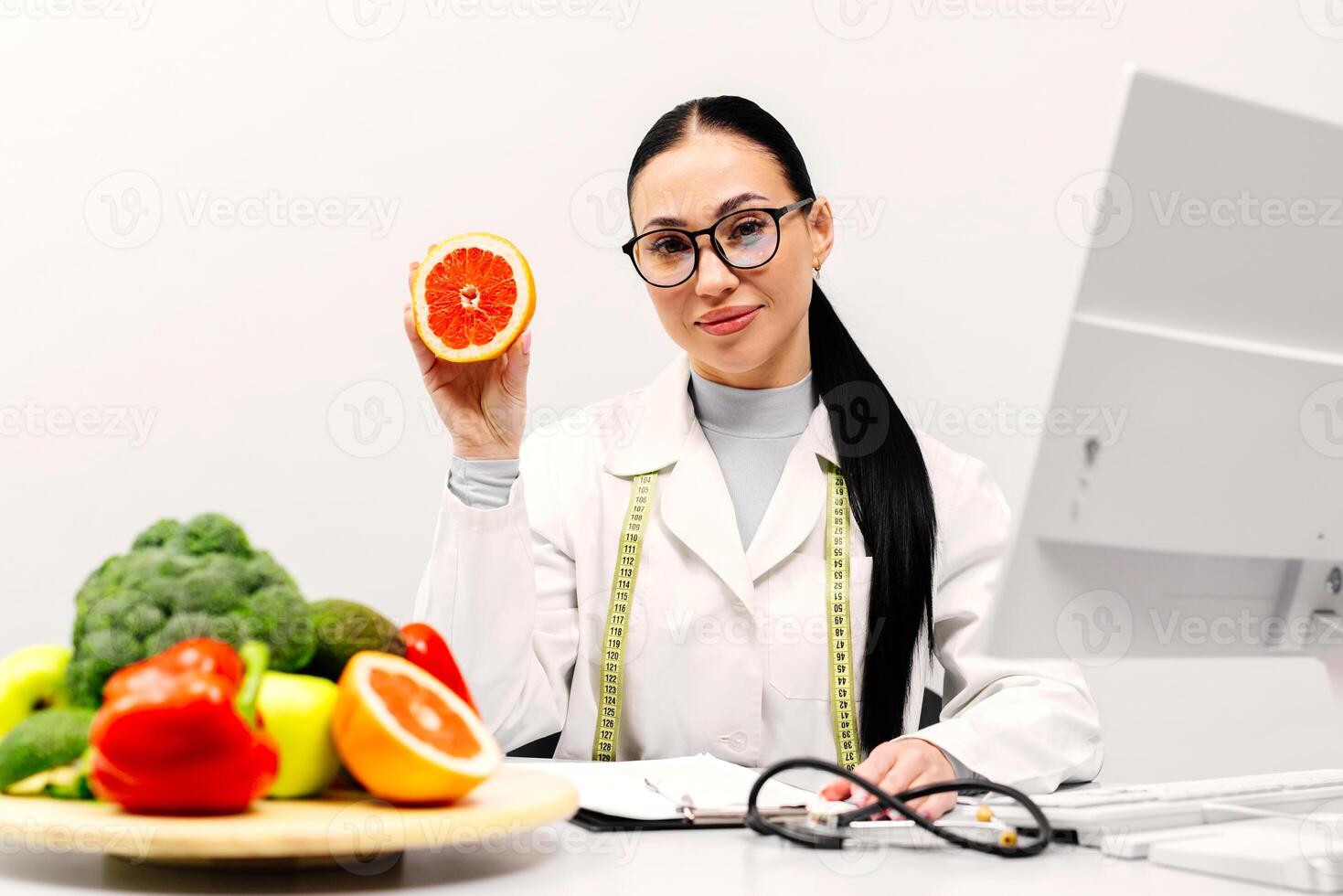 Cheerful young lady doctor in uniform pointing finger fruit isolated on light background, smiling at camera. Health care, diet, nutritional, advice from nutritionist photo