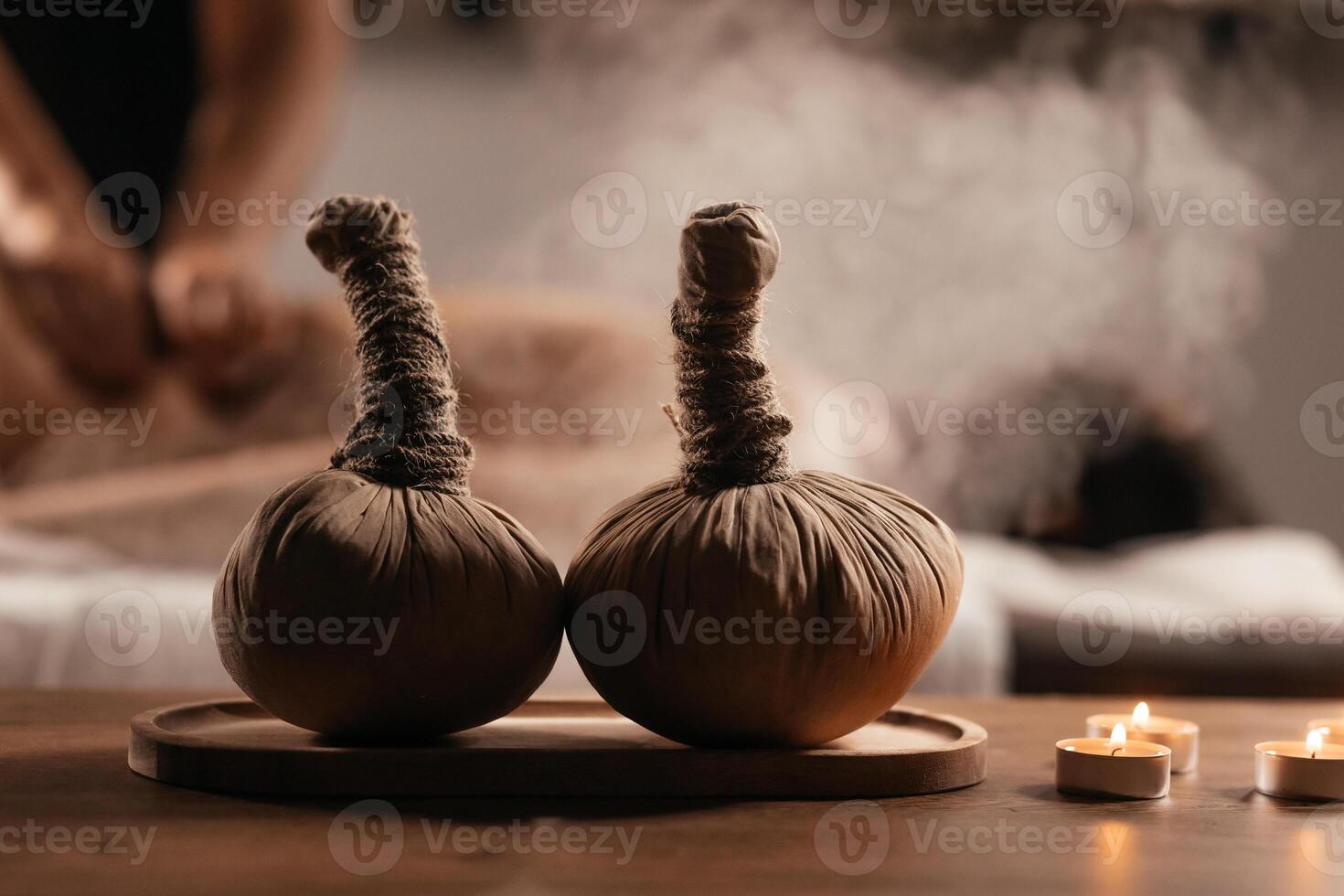 Thai Massage, asian woman in spa. Female having massage with herbal compress balls, hot steam in therapy spa salon. Blurred background. Close-up compress balls on a table with candles. photo
