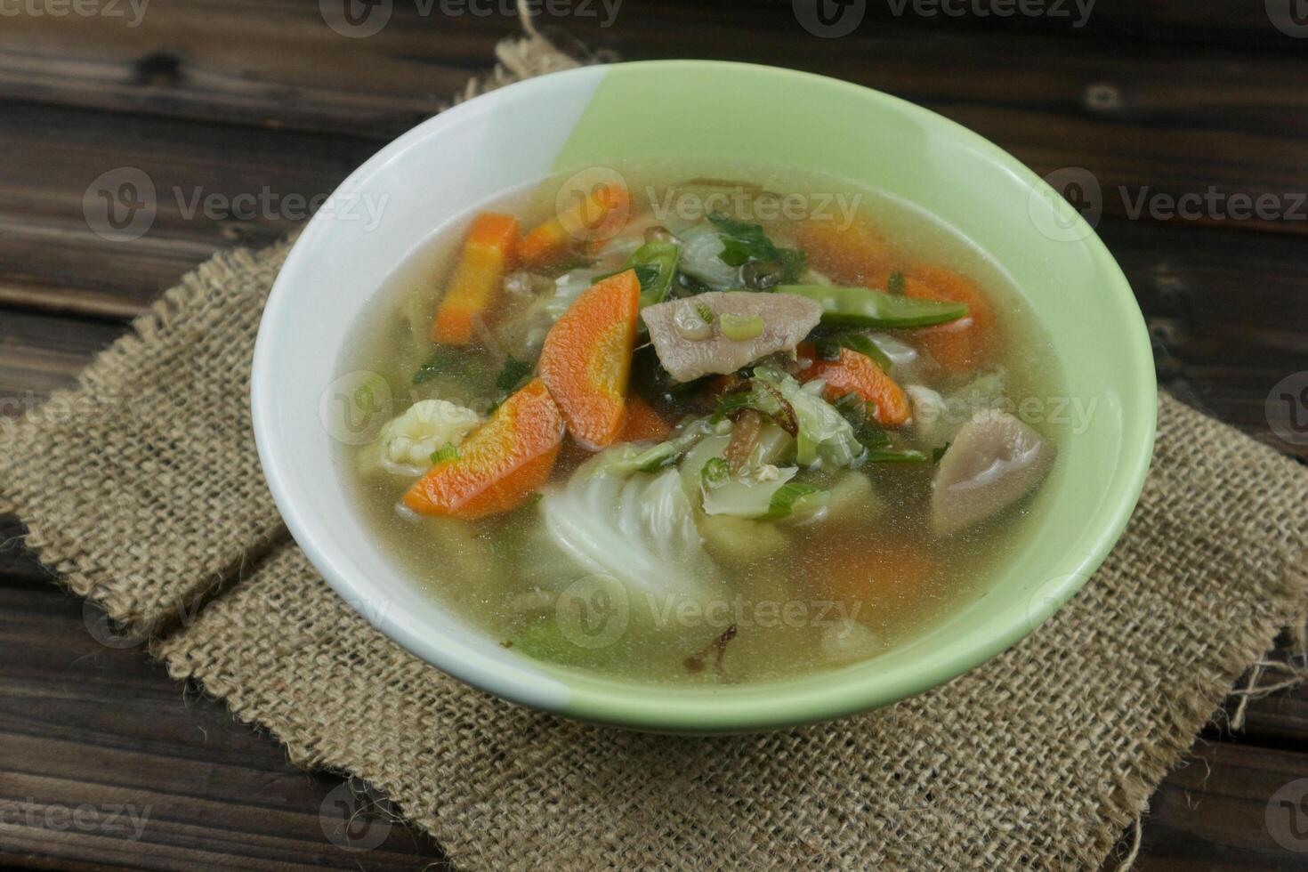 Vegetable soup with cauliflower, meatball, white cabbage, carrots and green peas on wooden background. photo
