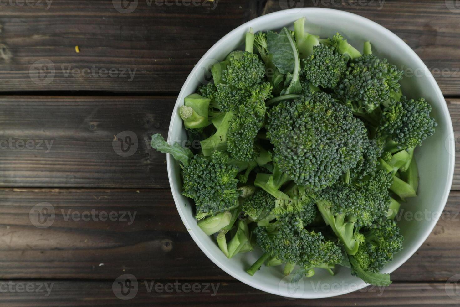 Fresh green broccoli in bowl on wooden background, table top view, empty space photo