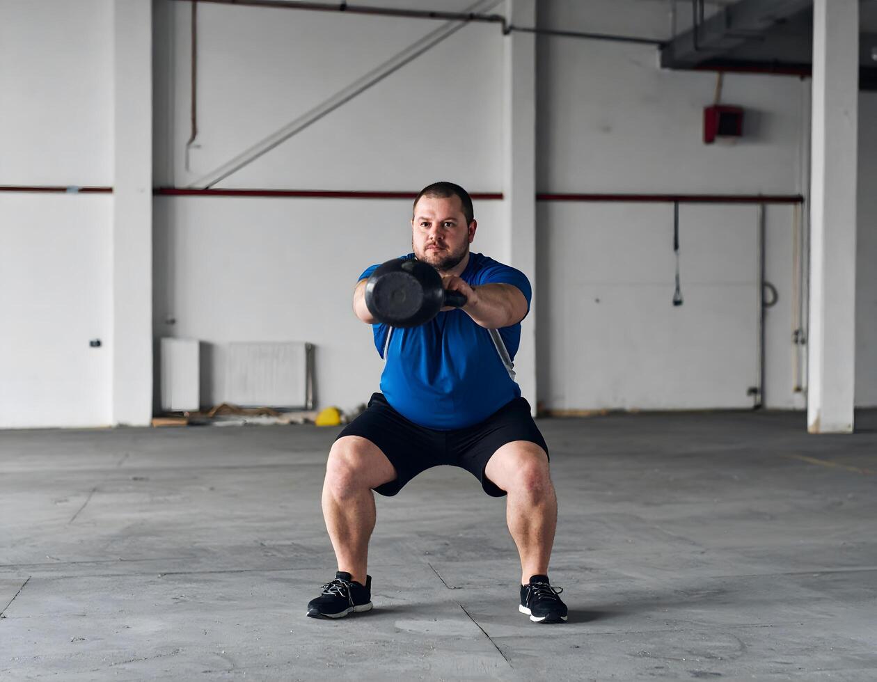 A plus-size man performing kettlebell squats in an empty garage with a rugged, industrial light vibe. photo
