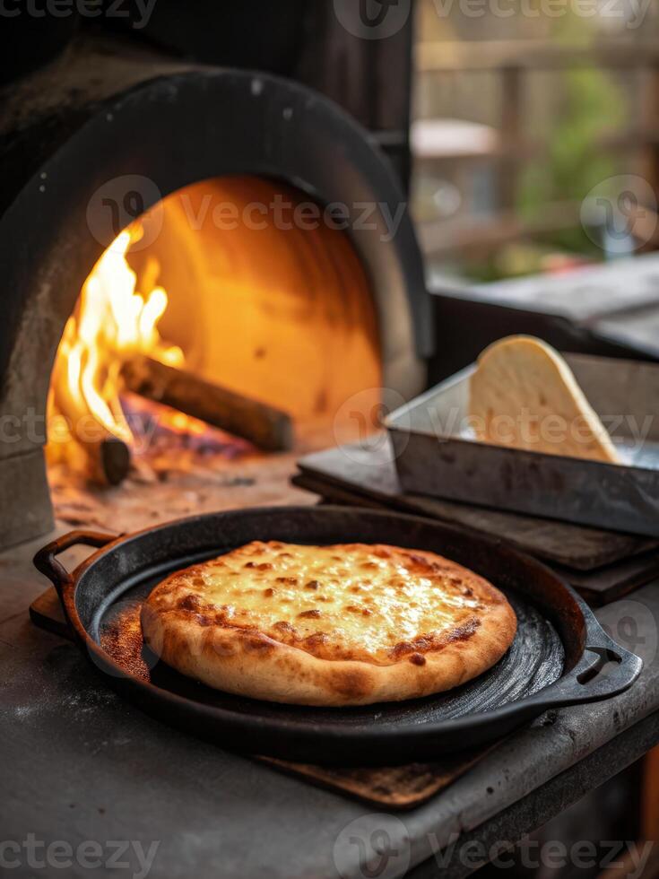 Khachapuri served on a cast iron tray beside a traditional wood fired oven photo