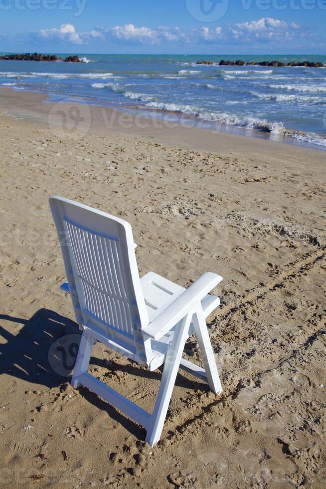 Deck chair next to water on an empty beach in winter photo