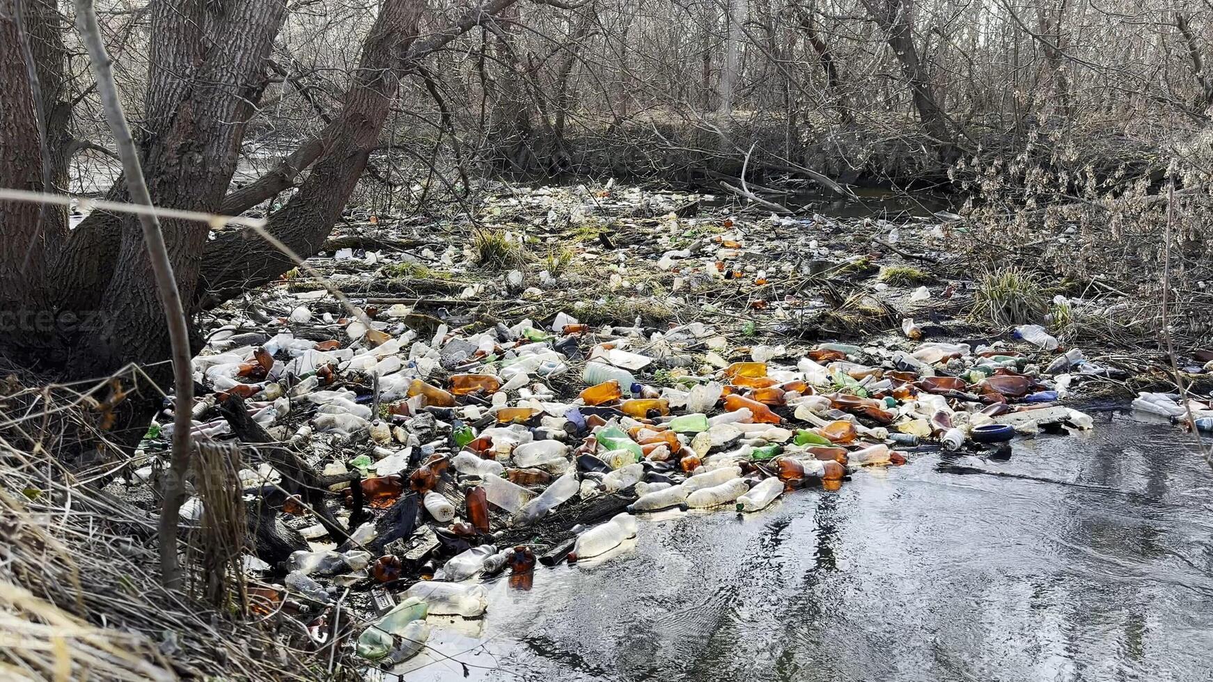 Dirty river is polluted with many plastic bottles. A lot of trash is dumped in open and freely available places at nature. Global environmental pollution problem. Concept of ecological disaster. photo