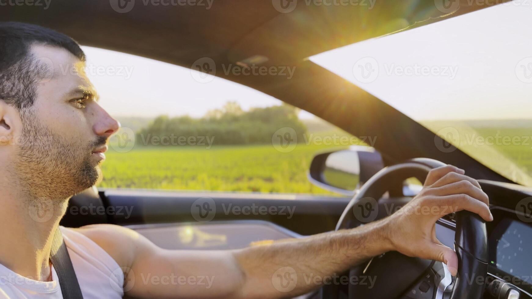 Profile of handsome man driving a modern electric car with sunlight at background. Young male driver riding on electrical vehicle at countryside. Concept of journey and trip. Close up photo