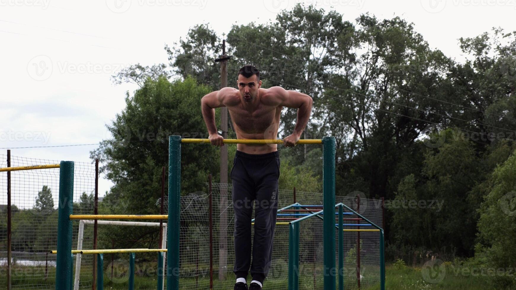 Hardy shirtless sportsman doing push ups on horizontal bar at nature. Strong and muscular guy training at sports ground. Young athletic guy exercising outdoor. Concept of active and healthy lifestyl photo