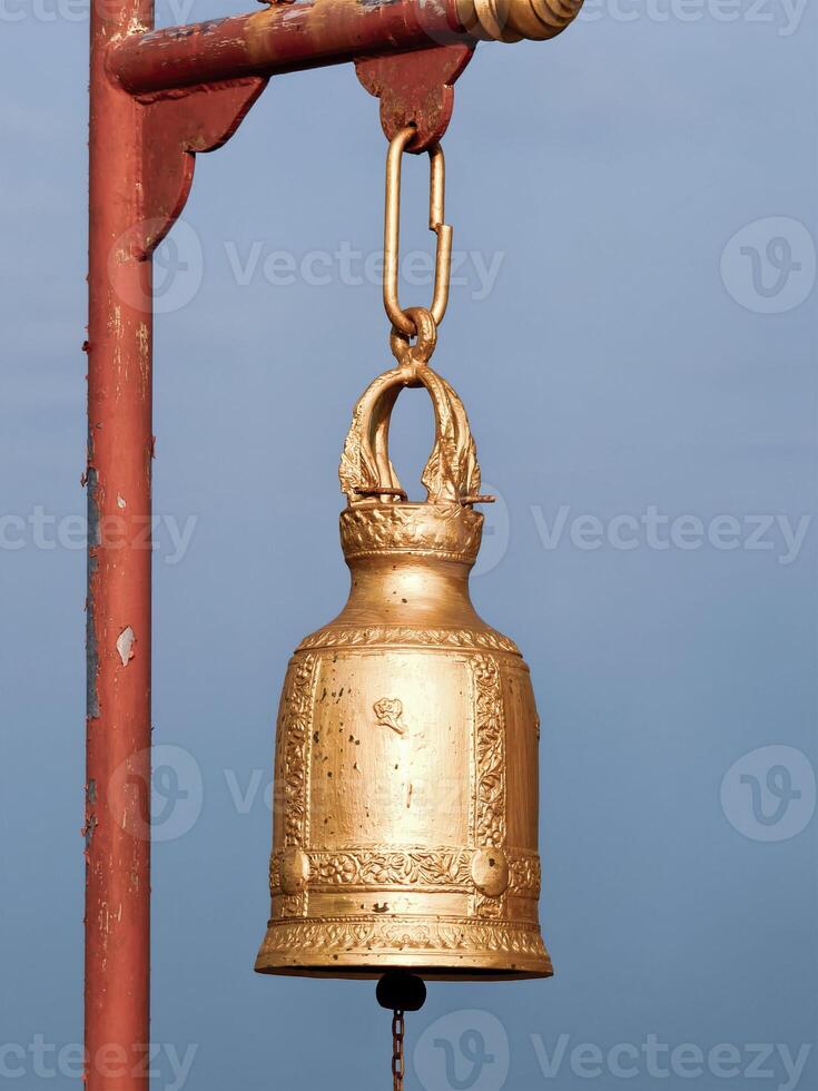 Golden Ornate Bell Hanging Against Clear Blue Sky on Rustic Metal Frame Capturing Serenity and Elegance photo