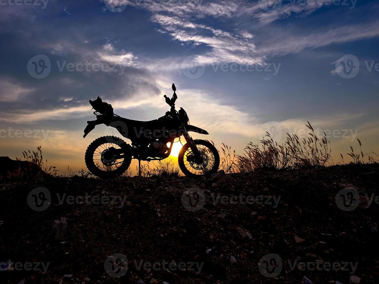 Silhouette of Motorcycle Against Dramatic Sunset Sky with Grassy Hill and Clouds in the Background photo