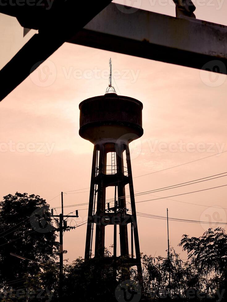 Silhouetted Water Tower Against a Warm Sunset Sky with Trees and Power Lines in the Foreground photo