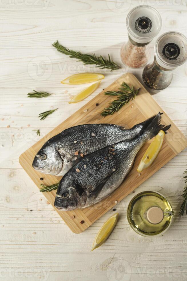 Fresh dorado fish with lemon, rosemary and spices on wooden cutting board, close up. Top view photo