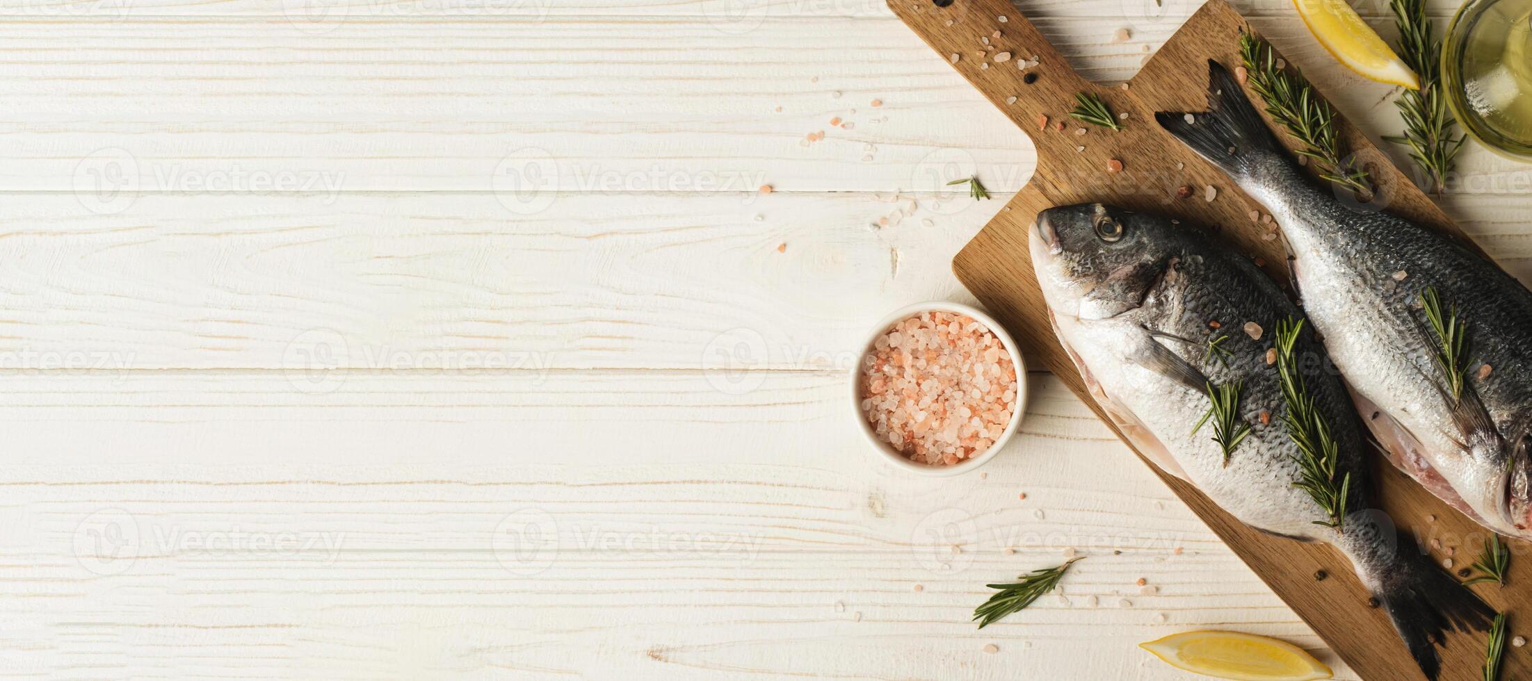 Fresh dorado fish with lemon, rosemary and spices on wooden cutting board, close up. Copy space photo