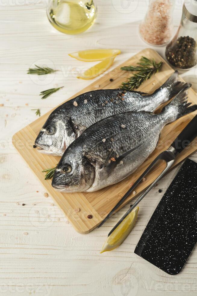 Raw Fresh dorado fish with lemon, rosemary and spices on wooden cutting board, close up photo