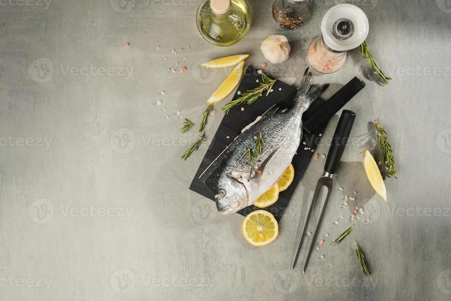 Fresh dorado fish with lemon, rosemary and spices on black cutting board photo