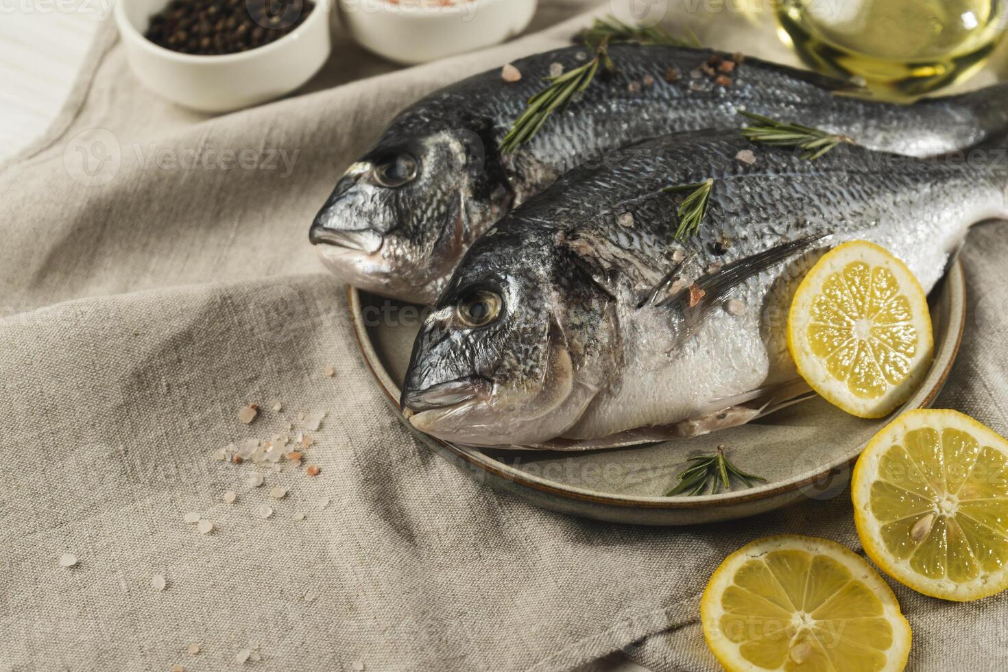 Raw Fresh dorado fish with lemon, rosemary and spices on a plate, close up photo