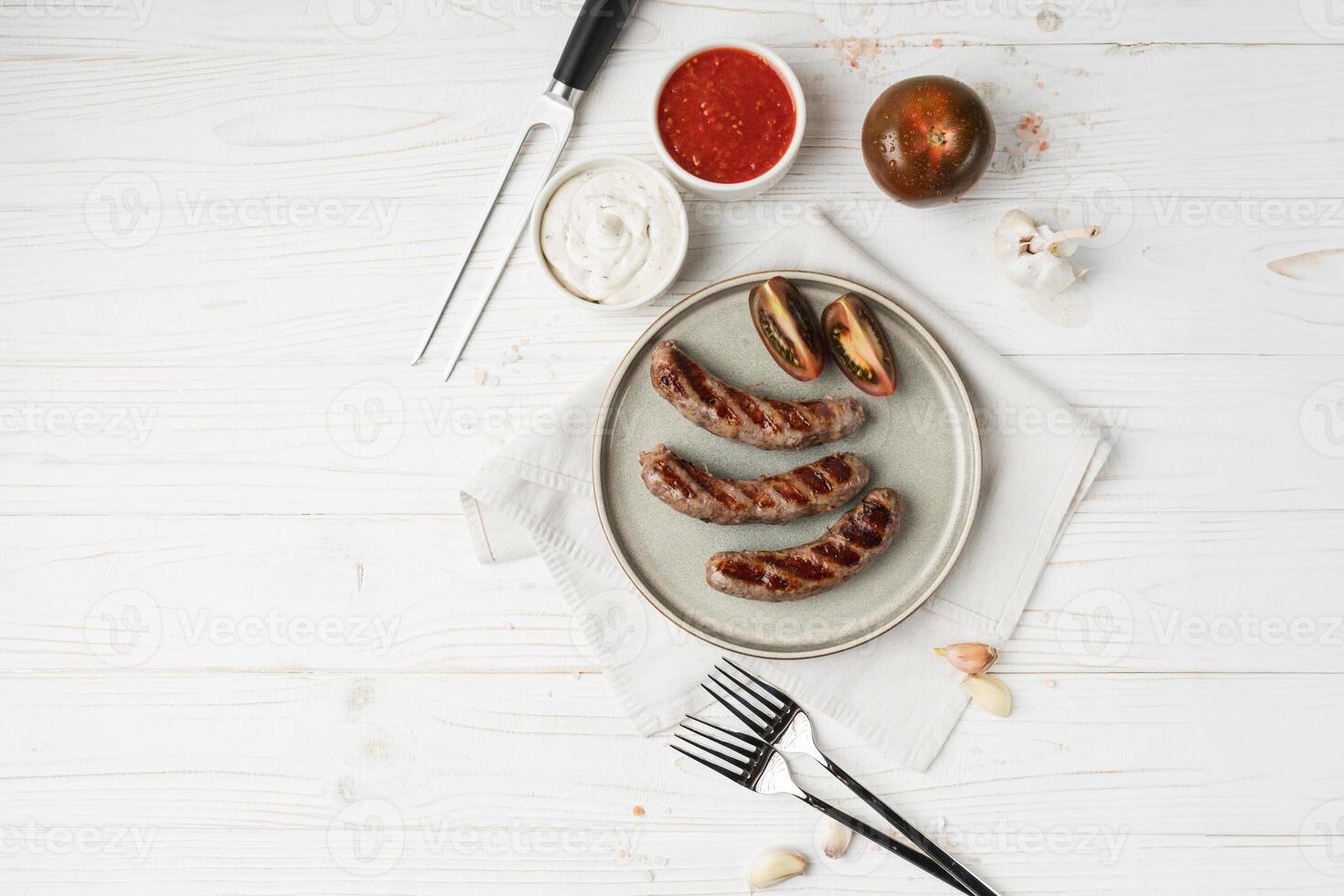 Flat lay of Ready to eat grilled sausages on the plate, white wooden background, close up. Concept of unhealthy eating photo