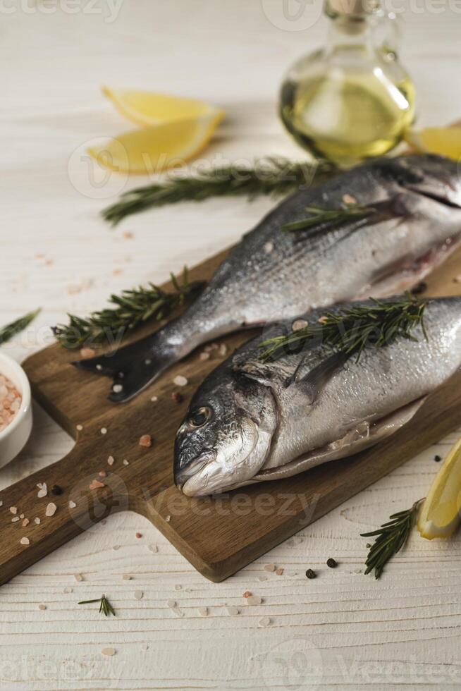 Fresh dorado fish with lemon, rosemary and spices on wooden cutting board, close up. Healthy eating photo