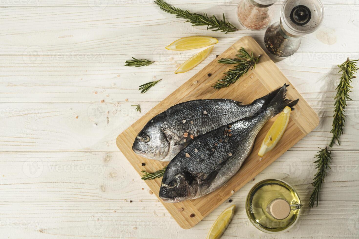 Fresh dorado fish with lemon, rosemary on wooden cutting board, close up photo