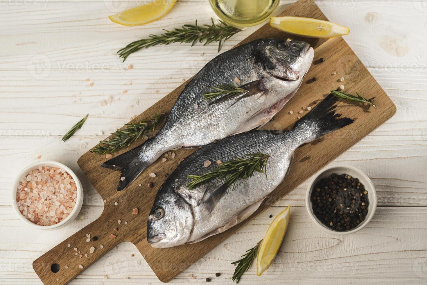 Flat lay of Fresh dorado fish with lemon, rosemary and spices on wooden cutting board, close up photo