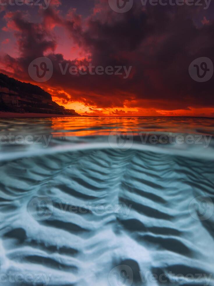 Sunset over calm sea with underwater sand patterns, captured in a split view seascape photo