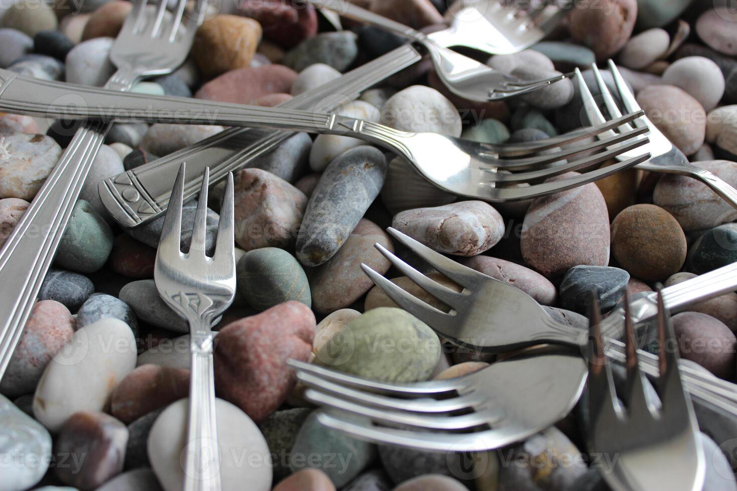 Same table forks and cake forks from the cutlery set scattered on colored pebbles photo