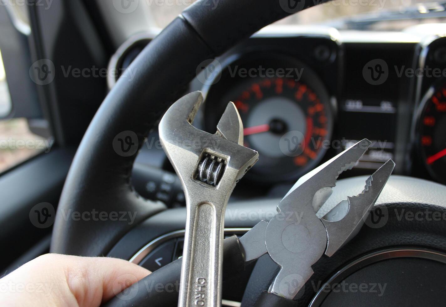 The driver holds in his hand set of tools for repair in front of the blurred car tachometer in vehicle with the ignition on photo