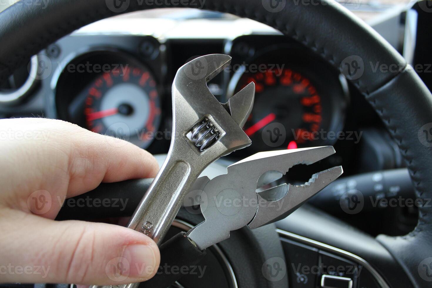 Pliers And Adjustable Wrench In Human Fingers In Front Of Defocused Car Dashboard With Red Digits And Arrows photo