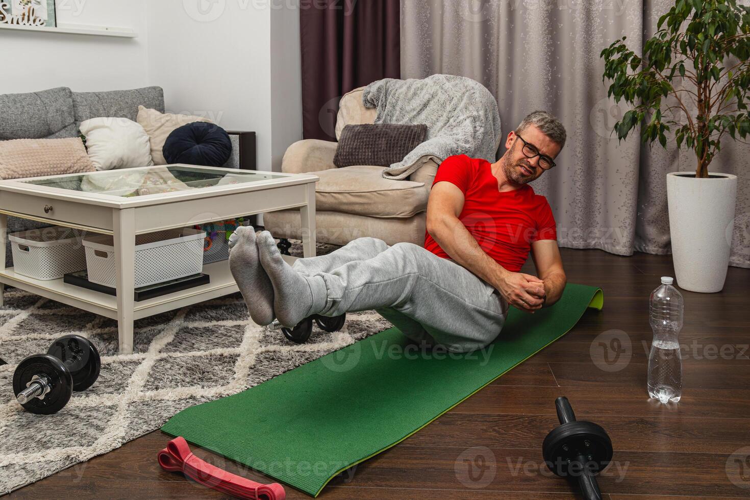 Man exercises at home on mat with dumbbells nearby photo