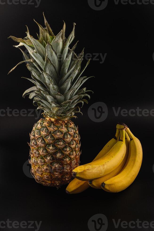 Fresh pineapple and ripe bananas on a dark background display natural colors photo