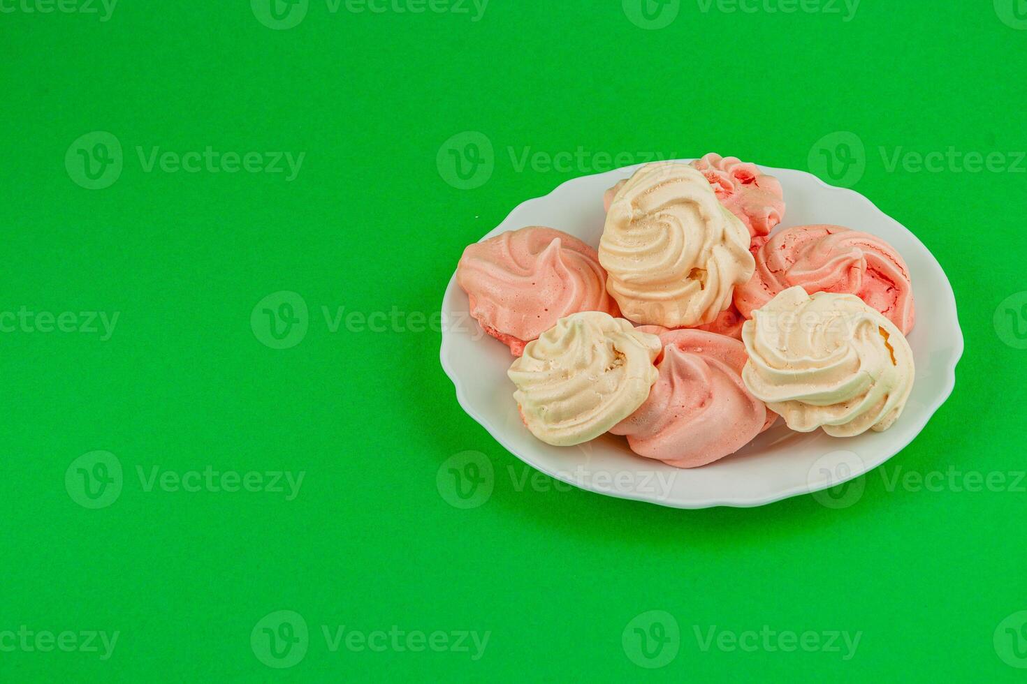 Colorful meringues arranged on a plate against a green background photo