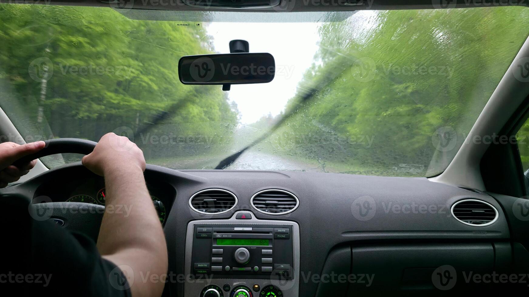 Driving in heavy rain. Interior view from the driver's seat. Wet windshield, blurred road and trees. Focus on the journey. Travel, transportation concept. photo