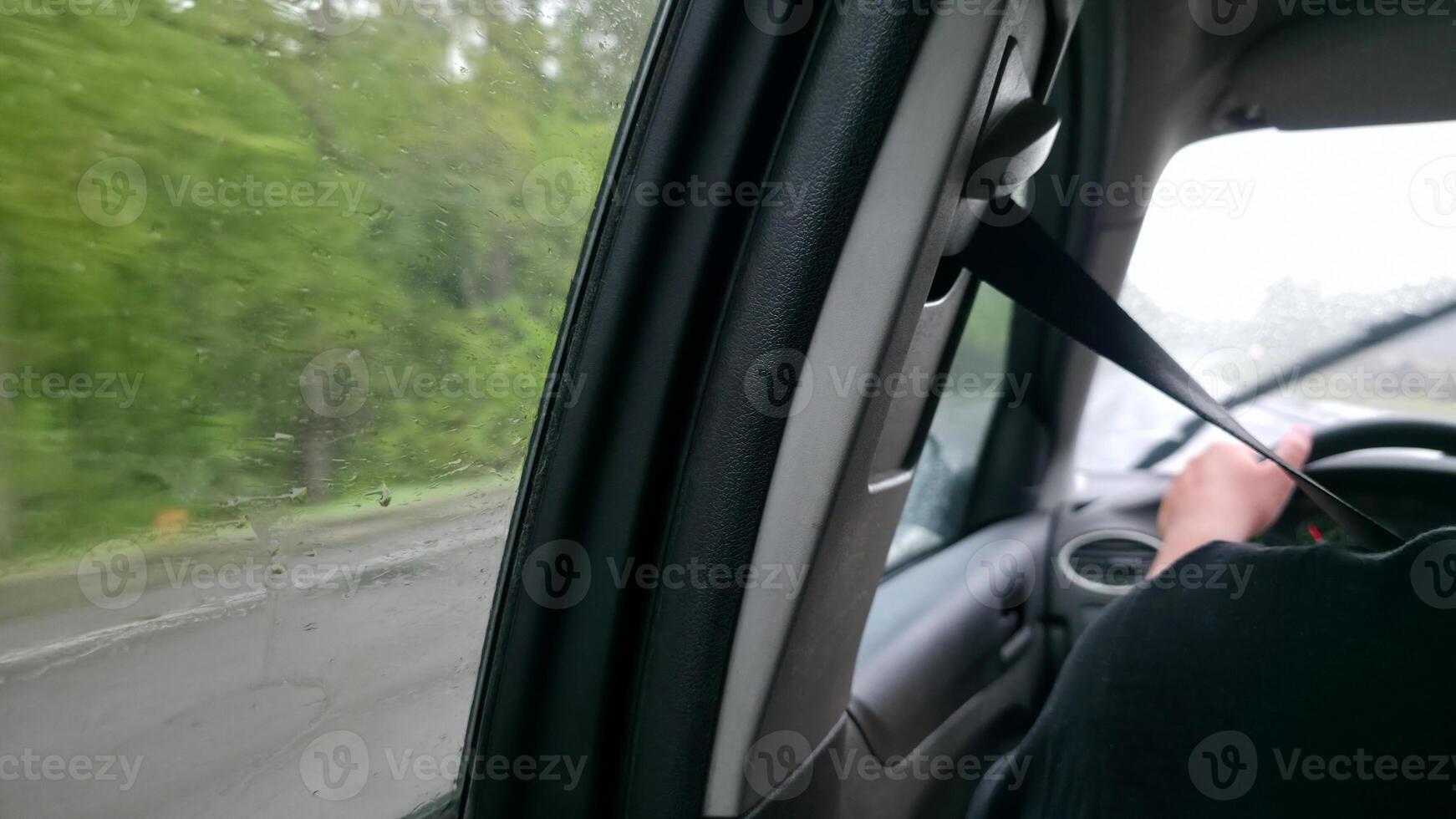 Driving in the rain. Interior view from the passenger seat. Wet window, blurred scenery. Focus on safety belt. Travel, transportation concept. photo