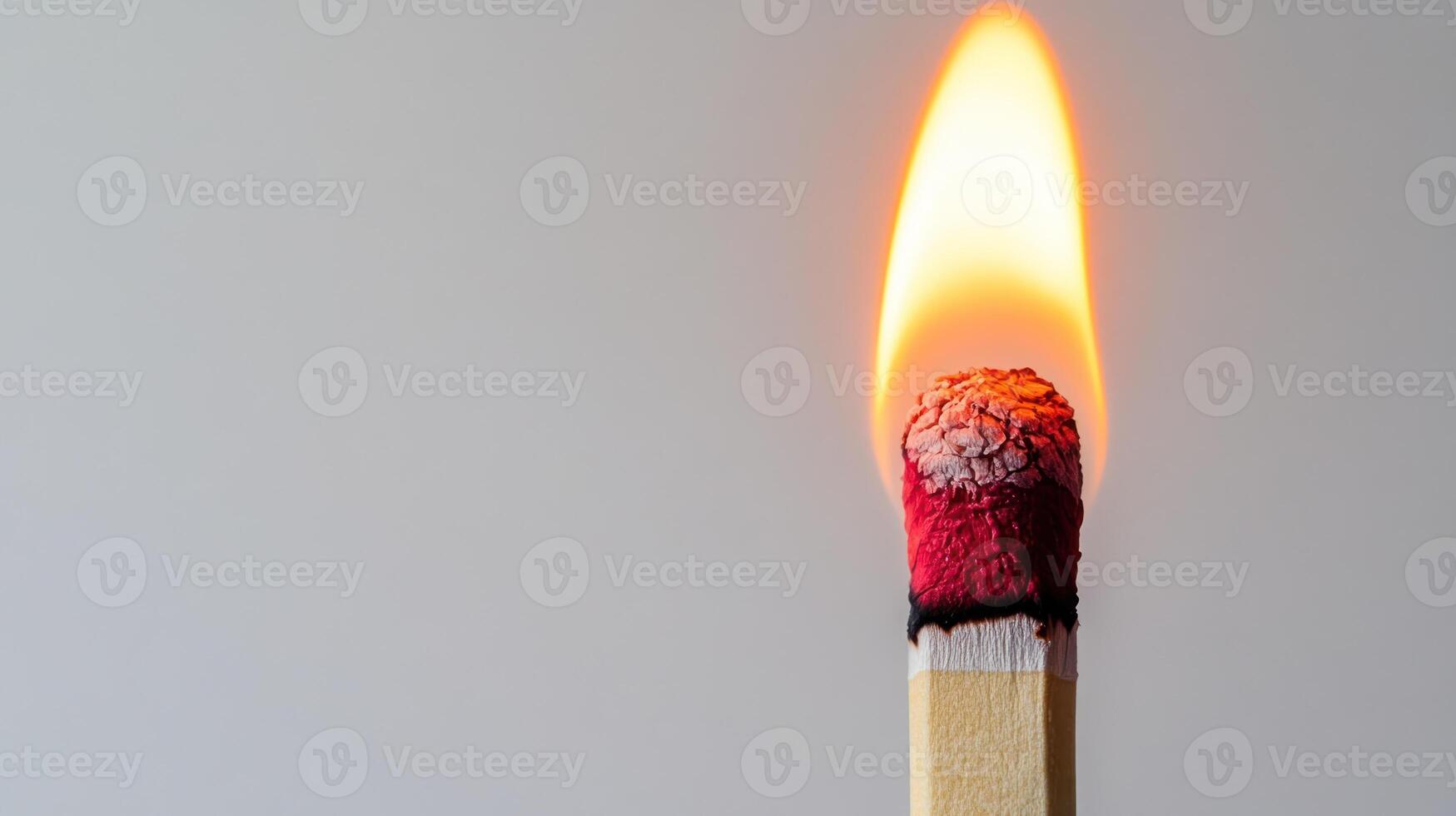 Close up of burning matchstick with bright flame and charred tip against plain light background, showing intense heat and energy photo