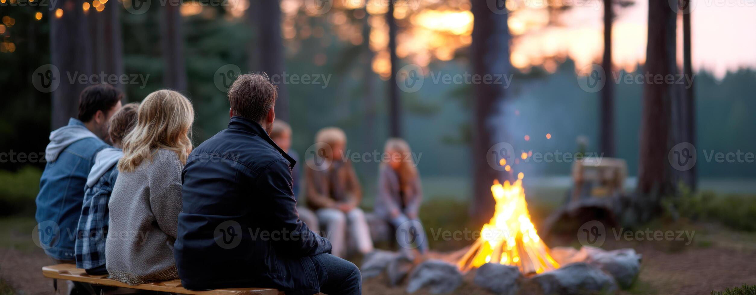 Group of people sitting on bench around campfire in forest during golden hour, enjoying warm and peaceful evening together photo