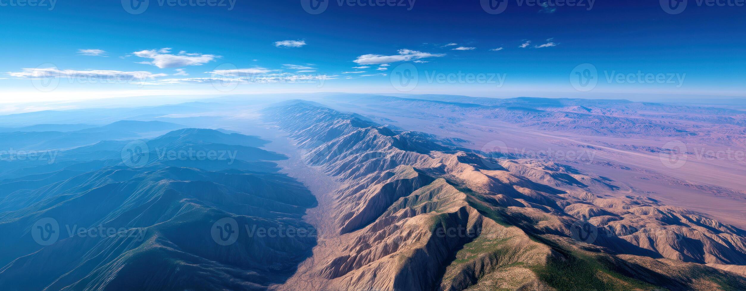 Aerial view of mountain range with rugged peaks and valleys under clear blue sky, showcasing natural beauty and vast landscape photo