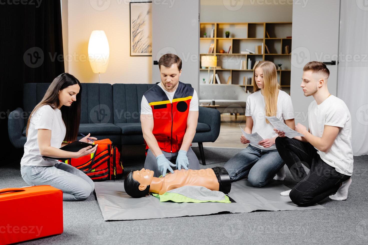 Young man instructor helping to make first aid heart compressions with dummy during the group training indoors. photo