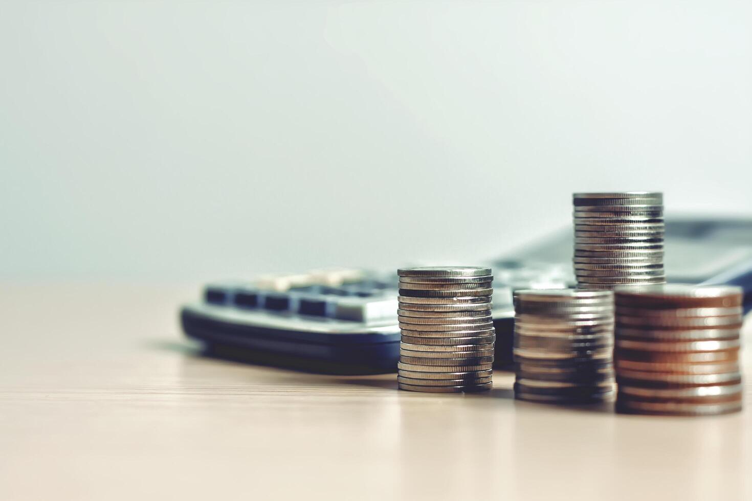 Money, coins stack, calculator and some stationery on wood table, On a bright background. Front view with copy space. Accounting and financial economic Math calculation concepts photo