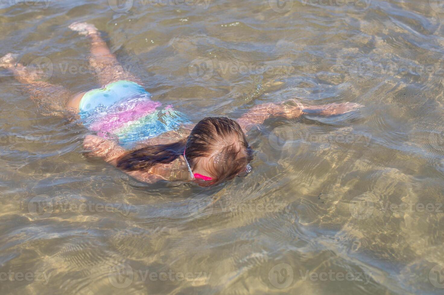 Young girl swimming in shallow water wearing colorful swimsuit. photo