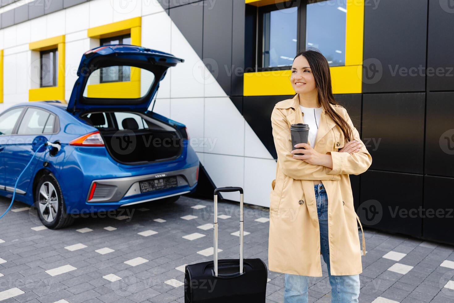 Young woman with cup of coffee waiting while her electric car charging, sustainable and economic transportation concept. photo