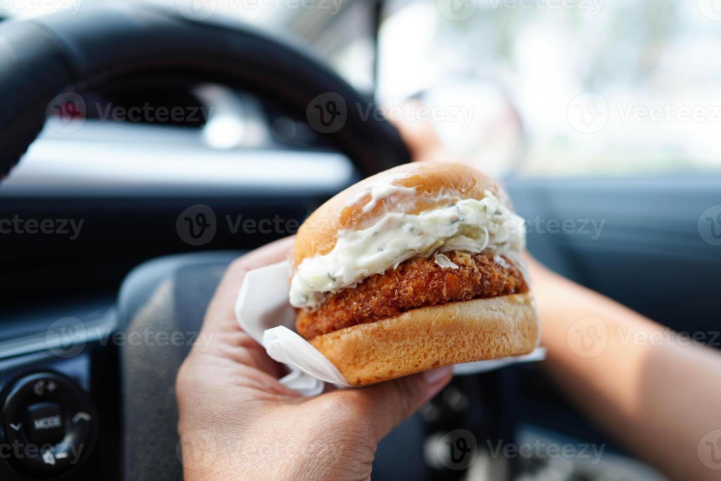 Asian woman driver hold and eat hamburger in car, dangerous and risk an acci photo