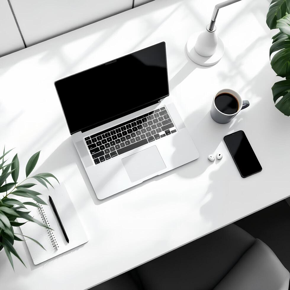 An overhead view of a white desk with a laptop, coffee cup and plant photo