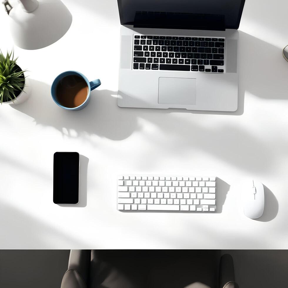 An overhead view of a white desk with a laptop, keyboard, mouse and coffee cup photo
