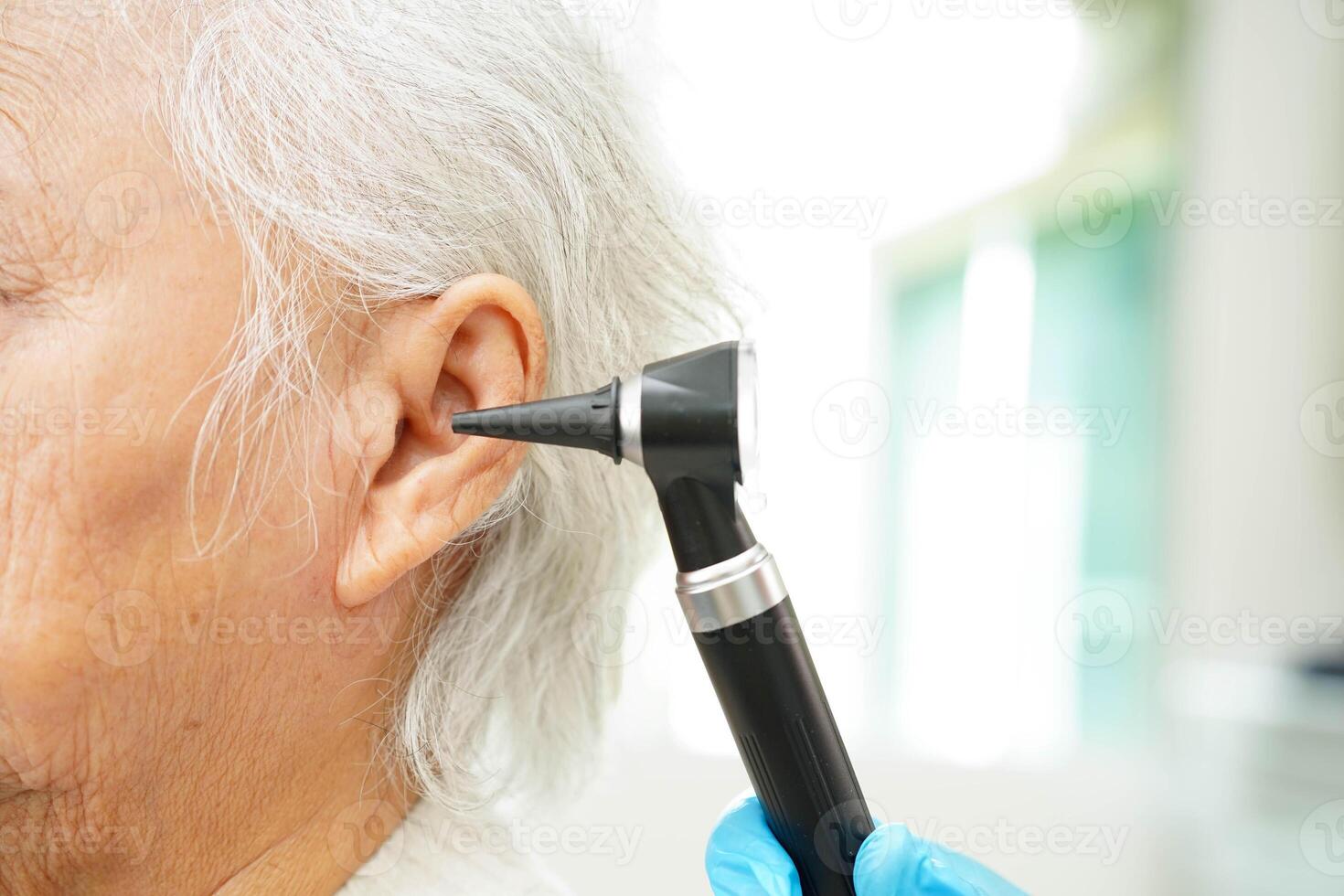 Otolaryngologist or ENT physician doctor examining senior patient ear with otoscope, hearing loss pro photo