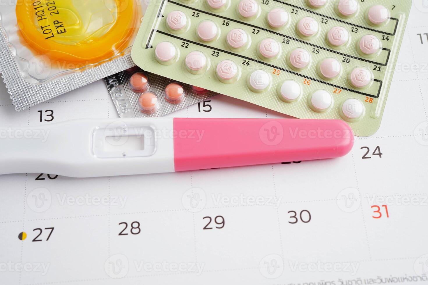 Pregnancy test with birth control pills and condom for female on calendar, ovulation photo