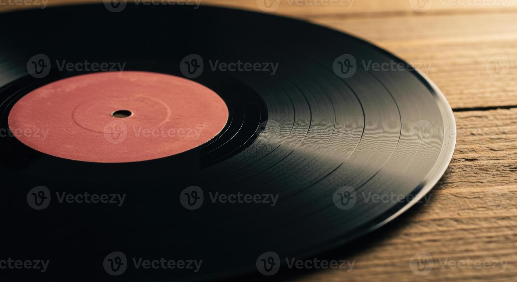 Close up of a slightly worn black vinyl record with a faded pink label on a rustic wooden surface. Warm lighting highlights the grooves. photo