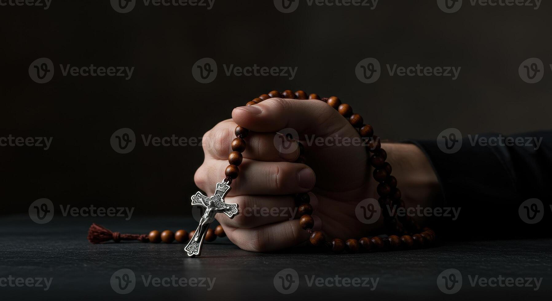Close up of a mans hand holding a wooden rosary with a silver cross on a dark surface, emphasizing faith and religious devotion. photo