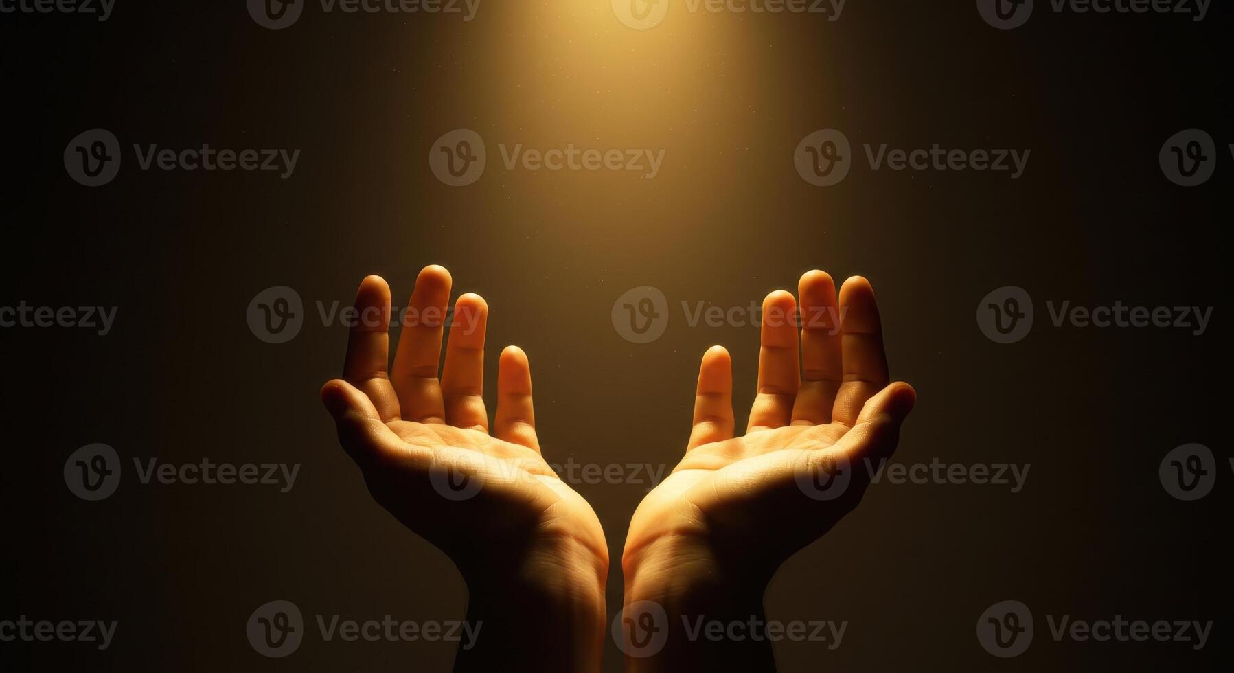 Two cupped hands reaching upwards against a dark background. A soft warm golden light emanates from above, gently illuminating the hands. photo