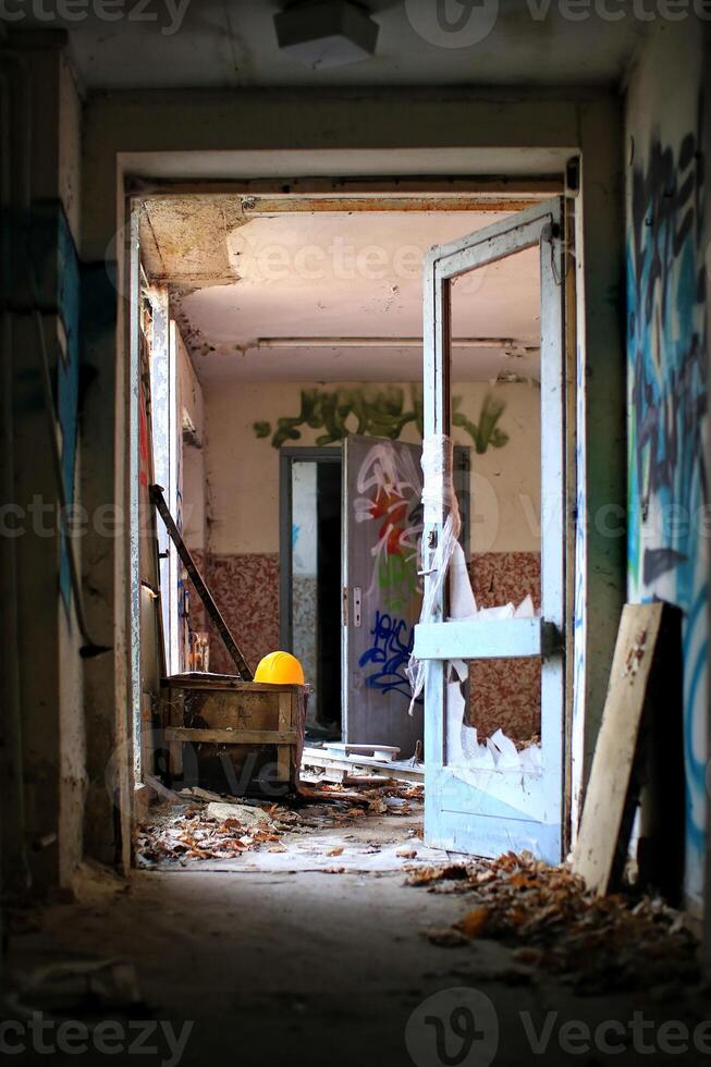 Broken doorway leading through an abandoned building with yellow helmet and scattered debris photo